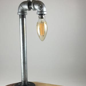May include: A table lamp made from galvanized pipe and a wooden slab base. The lamp has a single bulb and a black cord.