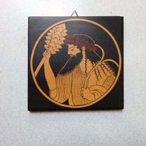 May include: Square wooden plaque with a classical Greek illustration. It shows a bearded figure holding a wheat stalk, within a circular frame. The color scheme includes black, tan, and red accents, with a gold-coloured border.