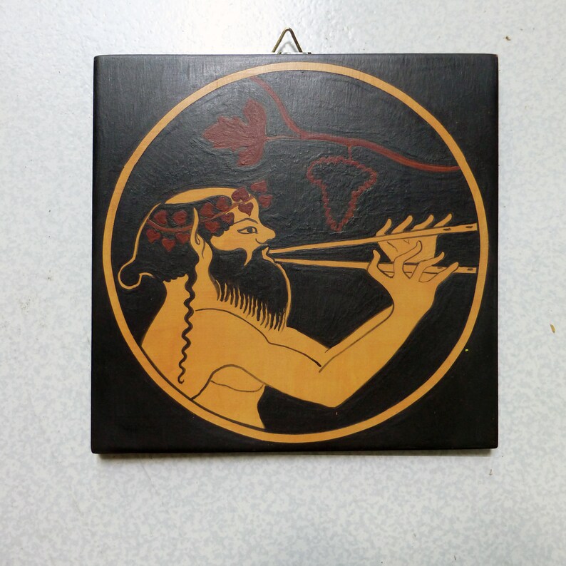 May include: Square, black wooden plaque with a circular design featuring a figure playing a wind instrument. The figure is in tan with red accents, set against a black background with a gold border. A red vine design is above the figure.
