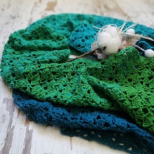 May include: A green and teal crocheted blanket with a white cotton flower on top.