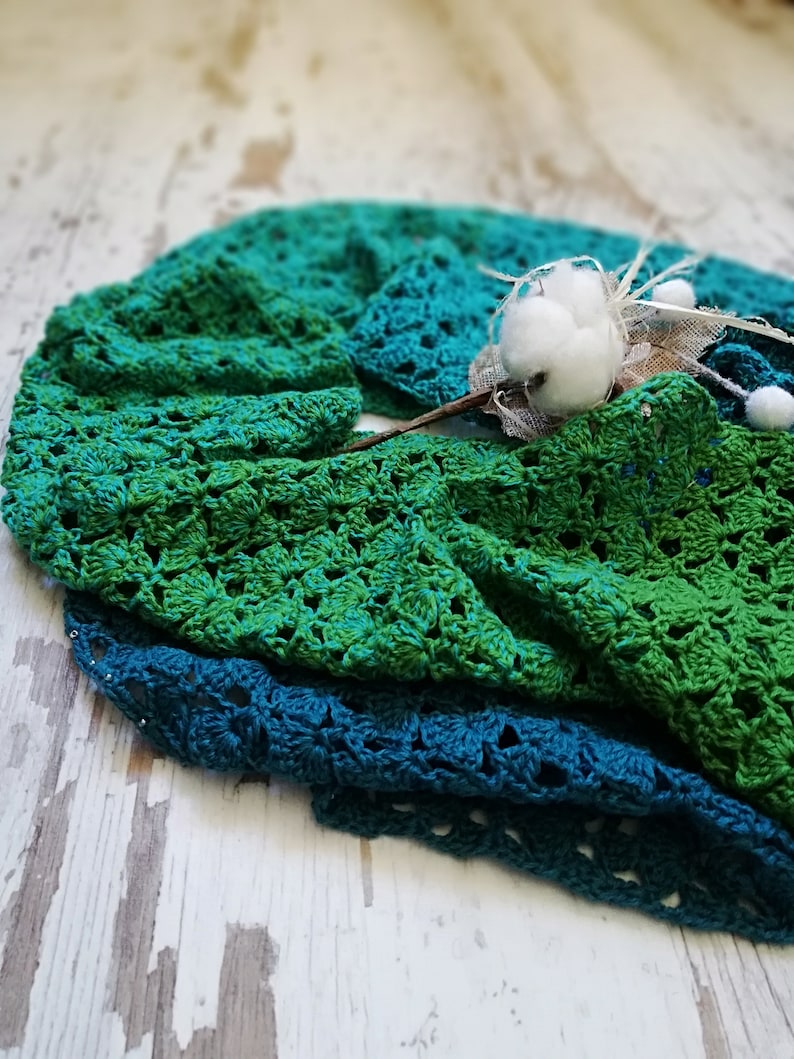 May include: A green and teal crocheted blanket with a white cotton flower on top.