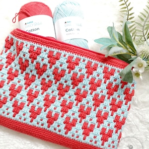 May include: A red and blue crocheted zippered pouch with a heart pattern. The pouch is filled with two balls of yarn, one red and one blue. The yarn labels read "Daily Stitch Cotton" and "Daily Stitch Cotton 100% Cotton".