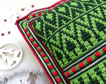 May include: Green and red crocheted pillow with a geometric pattern and white accents. The pillow has a border of red and white pom-poms.