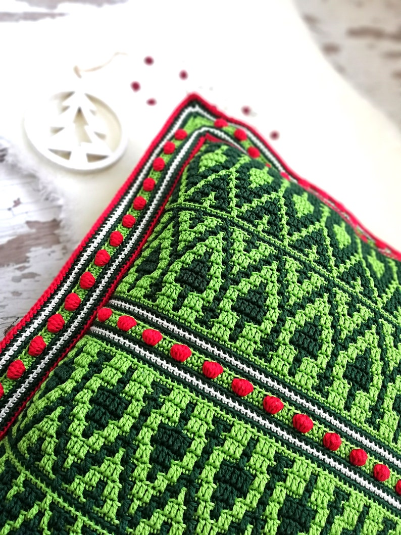 May include: Green and red crocheted pillow with a geometric pattern. The pillow has a white border with red pom-poms.