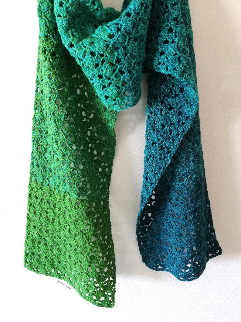 May include: A crocheted scarf with a gradient of green and teal colors. The scarf is made with a delicate open stitch pattern.
