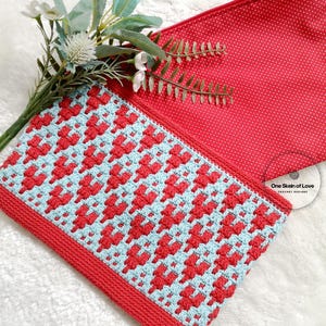 Puede incluir: Una bolsa de cremallera de ganchillo con un patr&oacute;n geom&eacute;trico rojo y azul. La bolsa est&aacute; hecha con un solo ovillo de hilo y tiene un forro de lunares rojos. La bolsa est&aacute; sobre una superficie blanca y peluda.
