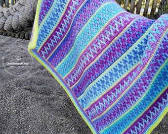 May include: A colourful crochet blanket with stripes of blue, purple, pink, and yellow. The blanket is made with a textured stitch and has a bright yellow border.