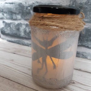 May include: A glass jar with a fairy silhouette inside, decorated with twine and glitter. The jar has a warm glow from a light inside.