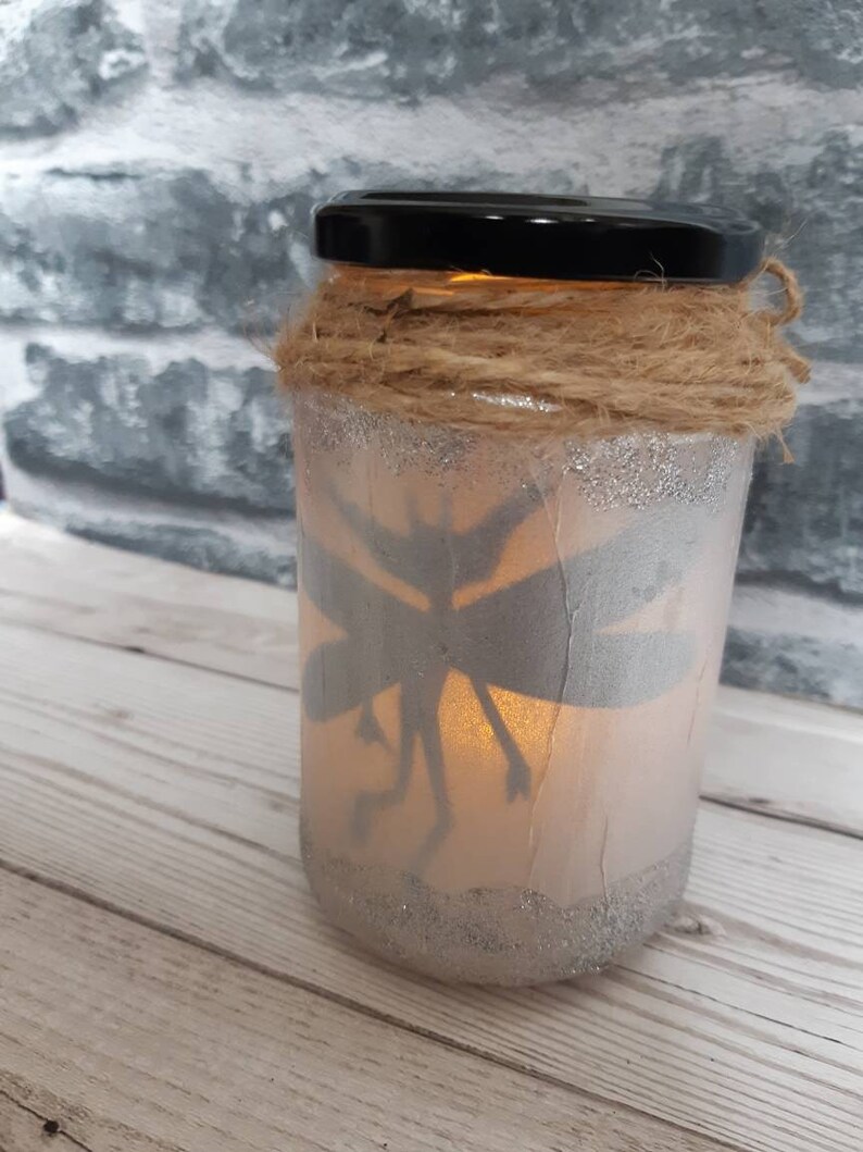 May include: A glass jar with a fairy silhouette inside, decorated with twine and glitter. The jar has a warm glow from a light inside.