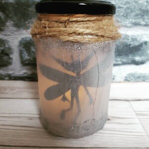 May include: A glass jar with a black lid, decorated with twine and glitter. The jar has a silhouette of a fairy inside, and is lit from within.