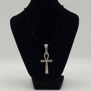 May include: A silver Ankh pendant necklace on a black cord. The pendant is a stylized cross with a loop at the top.