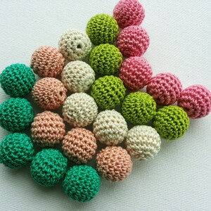 May include: A selection of small, crocheted balls in shades of green, pink, peach, and cream. The balls are tightly packed, highlighting their textured, handmade quality. Suitable for craft projects.