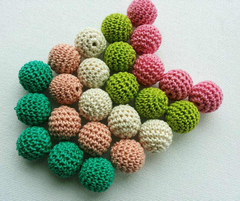May include: A selection of small, crocheted balls in shades of green, pink, peach, and cream. The balls are tightly packed, highlighting their textured, handmade quality. Suitable for craft projects.
