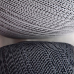 May include: Two spools of yarn, one gray and one dark gray. The yarn is wound tightly and has a textured surface.