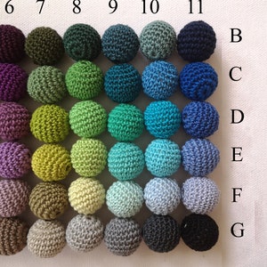 May include: Thirty-five crocheted spheres in a grid arrangement, showcasing a spectrum of colours. The spheres are organised in seven rows and five columns, with hues ranging from purple and green to blue and neutral shades like grey and brown. Each sphere has a handmade texture.