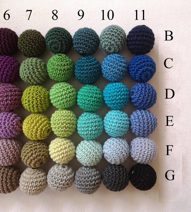 May include: Thirty-five crocheted spheres in a grid arrangement, showcasing a spectrum of colours. The spheres are organised in seven rows and five columns, with hues ranging from purple and green to blue and neutral shades like grey and brown. Each sphere has a handmade texture.