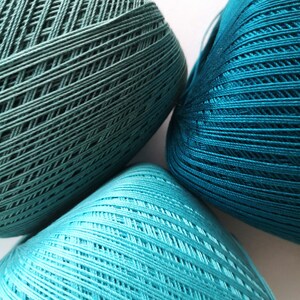 May include: Three balls of yarn in shades of teal and turquoise. The yarn is wound into balls and has a textured surface.