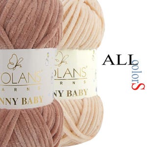 May include: Two skeins of Wolans Bunny Baby yarn, one in a dusty rose and one in a cream colour. Each skein features a white paper label with gold text reading Wolans Yarns Bunny Baby and a butterfly icon. The text ALL colours is visible.