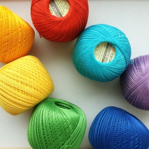 May include: A collection of colorful yarn balls in red, yellow, green, blue, and purple. Each ball has a label with the text "Yarns Lily" printed on it.