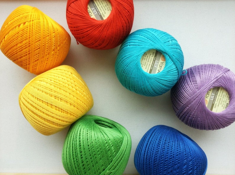 May include: A collection of colorful yarn balls in red, yellow, green, blue, and purple. Each ball has a label with the text "Yarns Lily" printed on it.