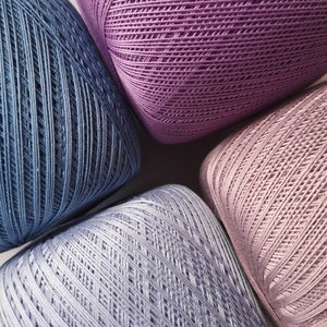 May include: Four balls of yarn in different shades of blue and purple. The yarn is a soft, textured material and is perfect for knitting or crocheting.