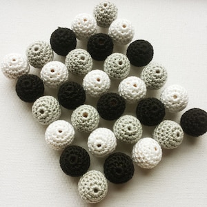 May include: A collection of crocheted beads in black, white, and gray. The beads are arranged in a diamond shape on a white surface.