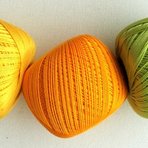 May include: Three balls of yarn in yellow, orange, and green. The yarn is wound into a ball shape and has a textured surface.