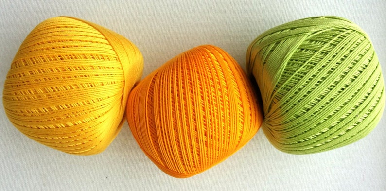 May include: Three balls of yarn in yellow, orange, and green. The yarn is wound into a ball shape and has a textured surface.