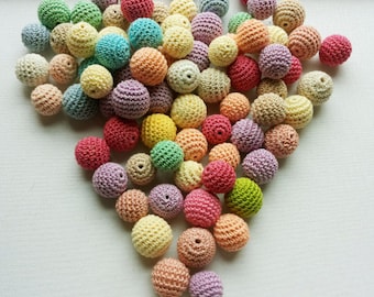 May include: A collection of colourful crocheted balls in various shades of pink, purple, yellow, green, and blue. The balls are arranged in a loose pile, creating a visually appealing and textured display.