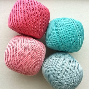 May include: Four balls of yarn in different colors: pink, light pink, teal, and light blue. The yarn is textured and has a woven look.