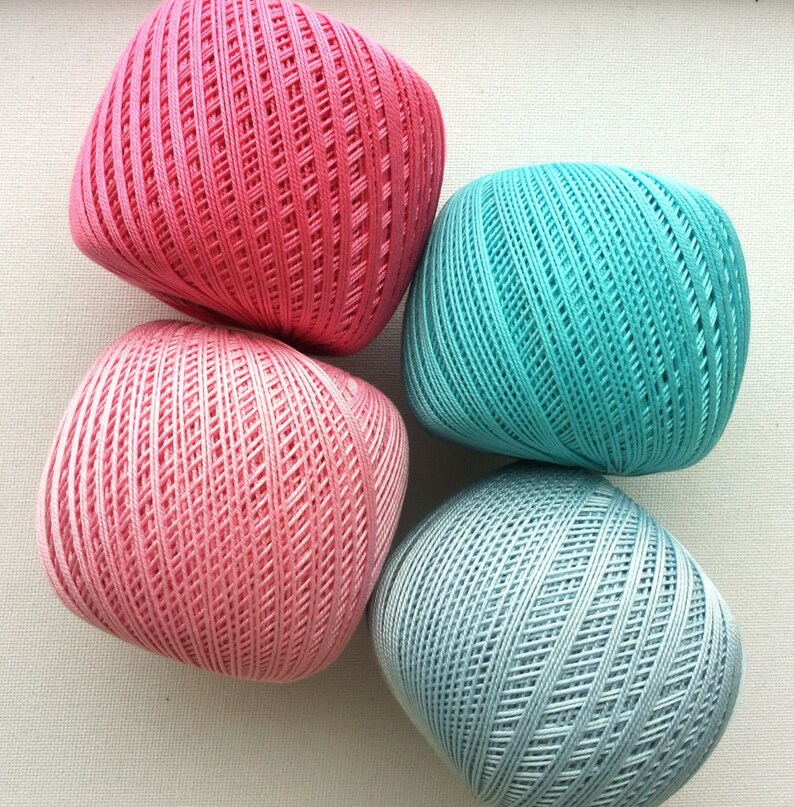 May include: Four balls of yarn in different colors: pink, light pink, teal, and light blue. The yarn is textured and has a woven look.