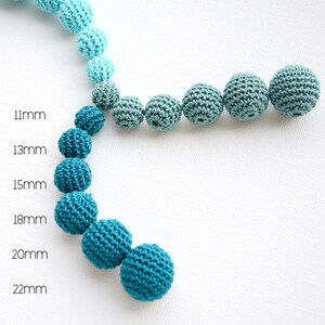 May include: A selection of crocheted beads in shades of blue and teal, with sizes from 11mm to 22mm. The beads are displayed in a curved line against a white backdrop, highlighting their size variations.