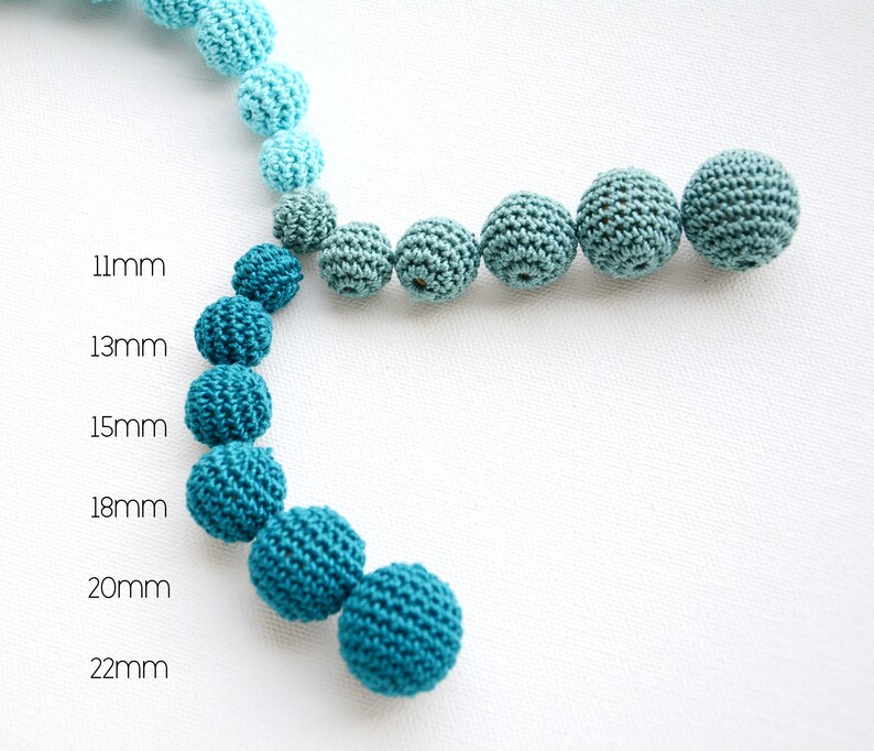 May include: A selection of crocheted beads in shades of blue and teal, with sizes from 11mm to 22mm. The beads are displayed in a curved line against a white backdrop, highlighting their size variations.