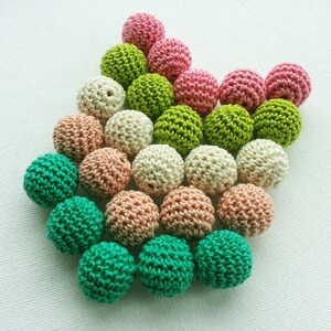 May include: A selection of crocheted balls in shades of pink, green, beige, and peach. The balls are arranged in a heart shape, highlighting their textured, handmade quality. The image is captured from a top-down angle, showing the details.