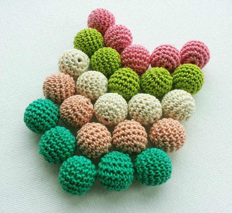 May include: A selection of crocheted balls in shades of pink, green, beige, and peach. The balls are arranged in a heart shape, highlighting their textured, handmade quality. The image is captured from a top-down angle, showing the details.