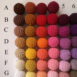 May include: A selection of crochet beads in a grid formation, showcasing a spectrum of colours. The beads vary from dark brown to white, including shades of orange, red, pink, and purple. Each bead is spherical, and the grid is labelled with numbers and letters.