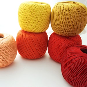 May include: Five balls of yarn in various shades of orange, red, and yellow. The balls are arranged in a pyramid shape.