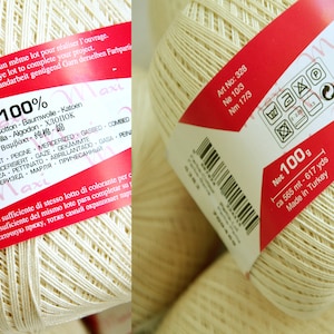 May include: A skein of white cotton yarn with a red and white label. The label reads "Maxi 100%" and includes information about the yarn's composition, care instructions, and origin. Art No: 328, No 10/3, Nm 17/3, Net 100g, ca 565 mt - 617 yds, Made in Turkey.