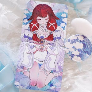 Puede incluir: Una colorida ilustración de un personaje de estilo anime con cabello rojo y alas de ángel, en una funda de teléfono. También se ve un botón redondo a juego con un diseño de nubes azules y blancas. El fondo presenta plumas blancas y cintas azules.