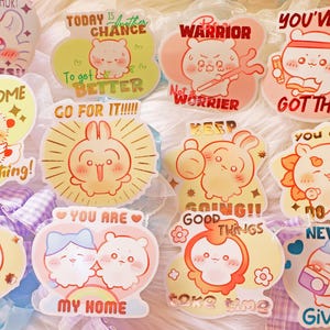 Puede incluir: Un conjunto de pegatinas coloridas con ilustraciones de animales lindos y frases motivadoras. Se pueden leer frases como «¡Puedes superarlo todo!» y «¡Nunca te rindas!». Las pegatinas están sobre un fondo suave y texturizado.