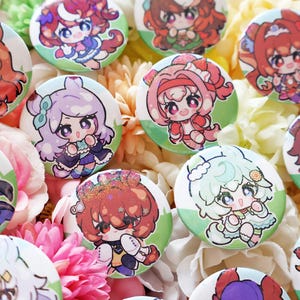 Puede incluir: Una colección de botones redondos y coloridos de personajes de estilo anime. Cada botón presenta un personaje diferente con ojos grandes y atuendos detallados, sobre un borde verde claro. Los botones están dispuestos sobre un lecho de flores.