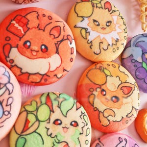 Pode incluir: Uma coleção de biscoitos redondos e coloridos decorados com desenhos de personagens de desenhos animados. Os biscoitos apresentam várias cores, incluindo laranja, amarelo, rosa, verde e roxo. Alguns biscoitos têm desenhos florais e de frutas. Outros produtos de panificação também são visíveis.