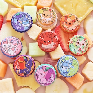 Könnte beinhalten: Eine Sammlung farbenfroher Flaschenverschlüsse mit Cartoon-Charakteren, umgeben von frischen Obstscheiben wie Erdbeeren, Ananas und Cantaloupe. Jeder Verschluss hat ein einzigartiges Design und den Text "Sweeten Your Day".