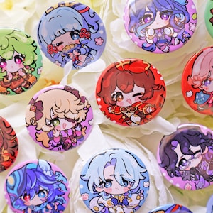 Puede incluir: Una colección de chapas circulares con ilustraciones coloridas de personajes estilo anime. Cada chapa muestra una figura única estilo chibi con colores de pelo, atuendos y rasgos faciales distintivos en un estilo artístico vibrante.