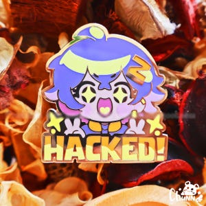 Peut inclure: Épinglette en émail doré représentant un personnage de dessin animé aux cheveux bleus et aux détails jaunes. Le texte "HACKED!" est écrit en lettres jaunes. Le fond est composé de fleurs séchées.
