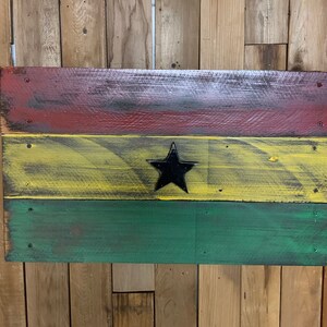 May include: A wooden sign painted with the colors of the Ghanaian flag. The flag is red, yellow, and green with a black star in the center.