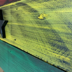 May include: A wooden sign painted in the colors of the Ghanaian flag. The sign features a black star in the center of the yellow stripe.