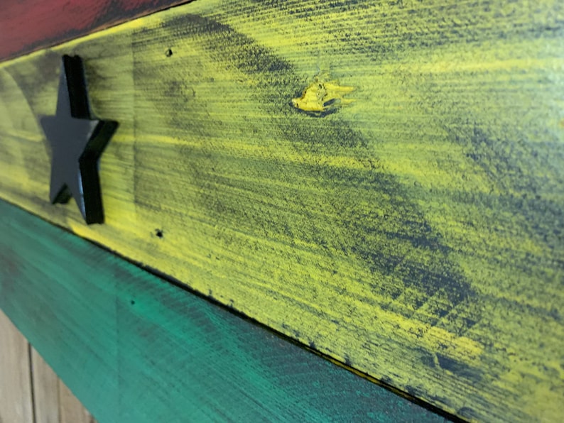 May include: A wooden sign painted in the colors of the Ghanaian flag. The sign features a black star in the center of the yellow stripe.