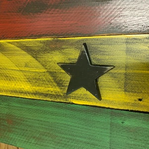 May include: A wooden sign painted in the colors of the Ghanaian flag. The sign features a black star in the center of the yellow stripe.