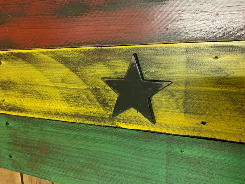 May include: A wooden sign painted in the colors of the Ghanaian flag. The sign features a black star in the center of the yellow stripe.